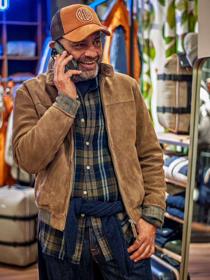 Hombre posando con chaqueta de cuero y pantalón oscuro frente a escaparate moderno.