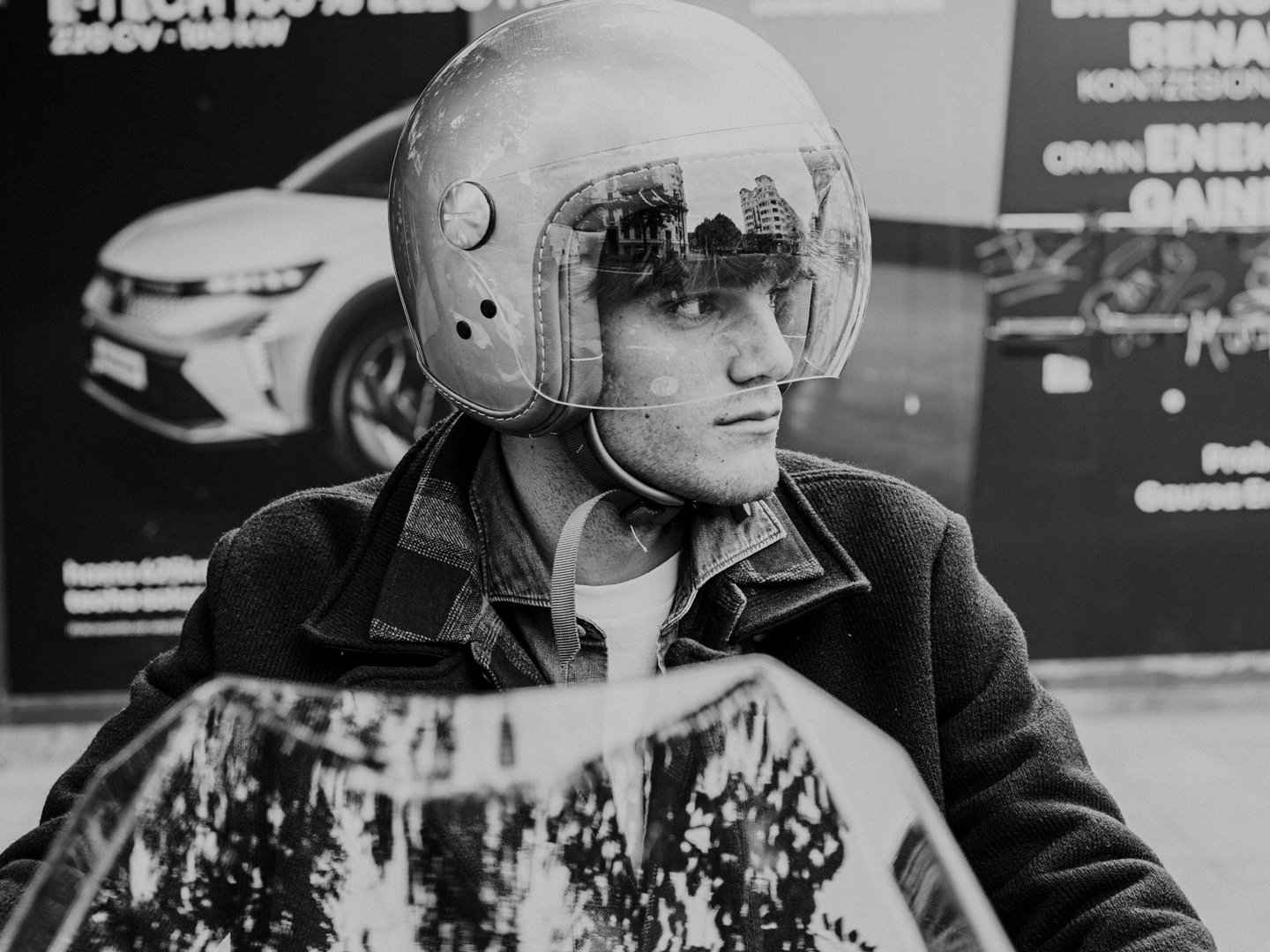 Hombre posando con chaqueta de cuero y pantalón oscuro frente a escaparate moderno.