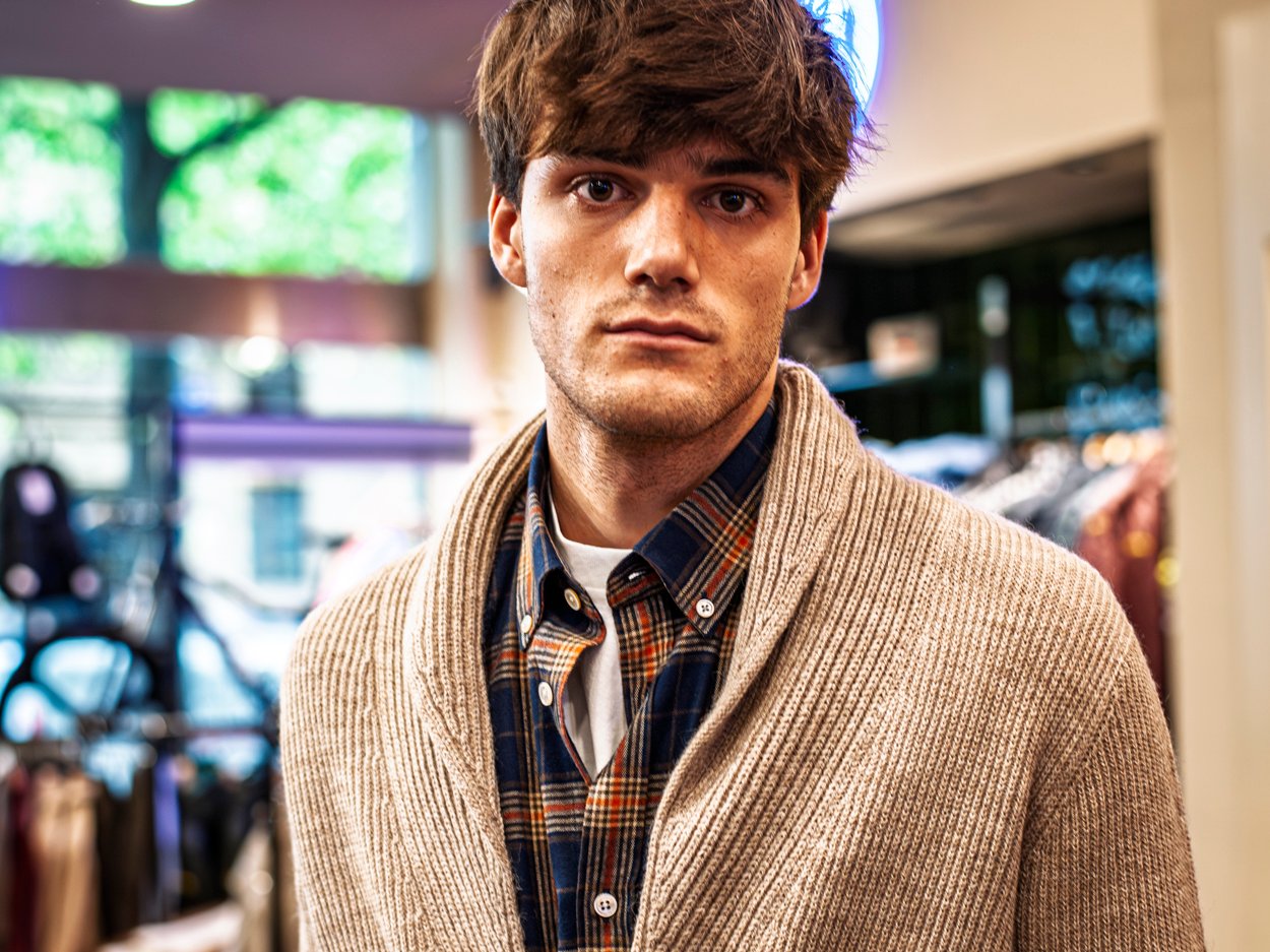 Hombre posando con chaqueta de cuero y pantalón oscuro frente a escaparate moderno.